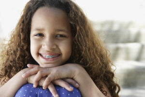 Smiling girl with braces leaning chin on knees outdoors